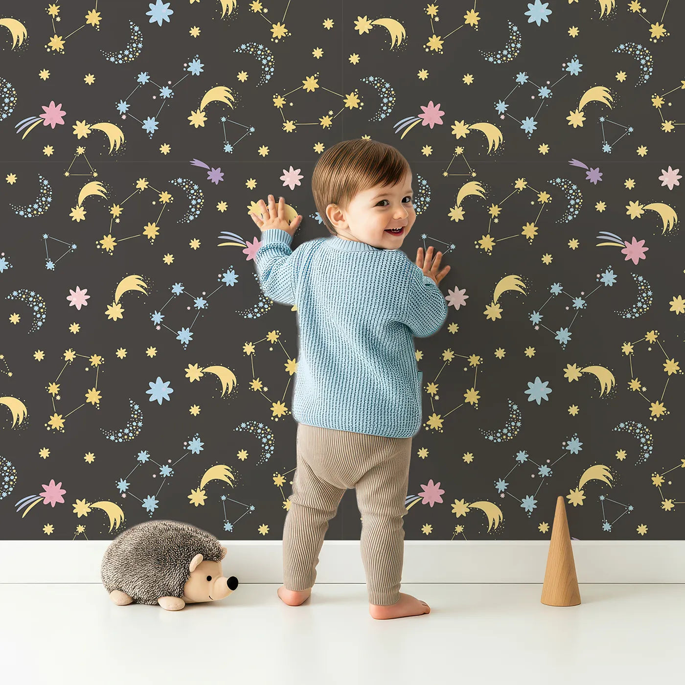 Lovely child standing in front of Whimsy Tots Starglow Constellation Dance Wallpaper in Charcoal Gray with moon, star, constellation, shooting star, galaxy in design.
