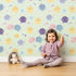Lovely child standing in front of Whimsy Tots Planet Pals Orbit Parade Wallpaper in Mint Green with planet, sun, moon, star, comet in design.