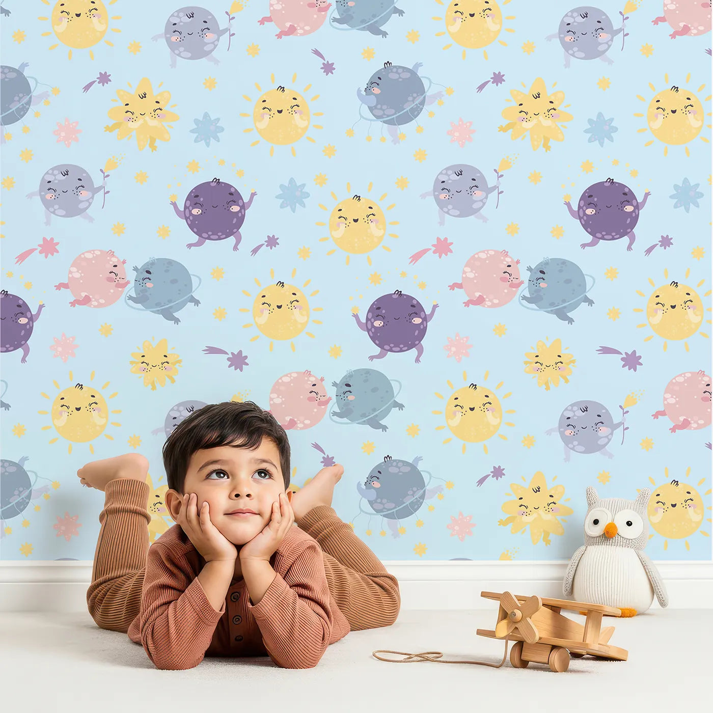 Lovely child standing in front of Whimsy Tots Planet Pals Orbit Parade Wallpaper in Sky Blue with planet, sun, moon, star, comet in design.