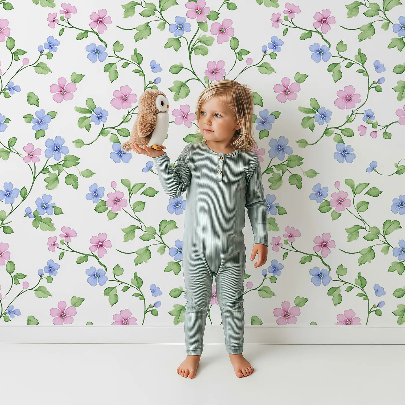 Lovely child standing in front of Whimsy Tots Dancing Meadow Blooms Wallpaper with flower, vine, leaf in design.