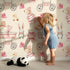 Lovely child standing in front of Whimsy Tots Tiny Tots Toy Parade Wallpaper in Cream with rabbit, bird, duck, bear, stroller, boot, toy, dress in design.