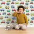 Lovely child standing in front of Whimsy Tots Tiny Wheels Parade Wallpaper in Mint Green with car, truck, bus, firetruck, ambulance in design.