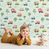 Lovely child standing in front of Whimsy Tots Bumper Buddies Forest Drive Wallpaper in Mint Green with car, tree, cloud, raindrop, bus in design.