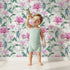Lovely child standing in front of Whimsy Tots Rosy Garden Stroll Wallpaper in White with rose, flower, stem, leaf in design.