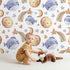 Lovely child standing in front of Whimsy Tots Starry Whale Drift Wallpaper in White with whale, moon, star, comet in design.