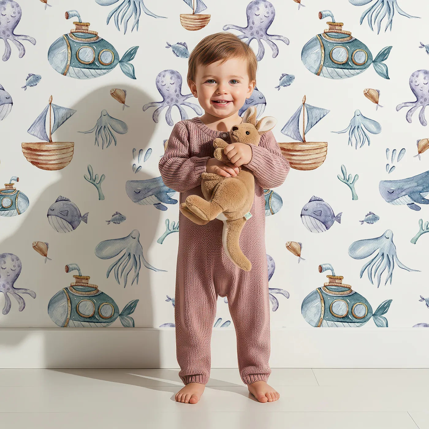 Lovely child standing in front of Whimsy Tots Undersea Slumber Voyage Wallpaper in White with whale, submarine, octopus, boat, fish in design.