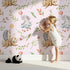 Lovely child standing in front of Whimsy Tots Starlight Forest Friends Wallpaper in Cream with rabbit, hedgehog, star, flower, leaf in design.