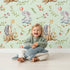 Lovely child standing in front of Whimsy Tots Starlight Forest Friends Wallpaper in Mint Green with rabbit, hedgehog, star, flower, leaf in design.