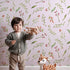 Lovely child standing in front of Whimsy Tots Blossom Meadow Breeze Wallpaper in Blush Pink with flower, leaf, vine, berry in design.