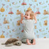 Lovely child standing in front of Whimsy Tots Wishful Woodland Friends Wallpaper in Sky Blue with hedgehog, owl, mouse, snail, mushroom, leaf, pumpkin, star in design.