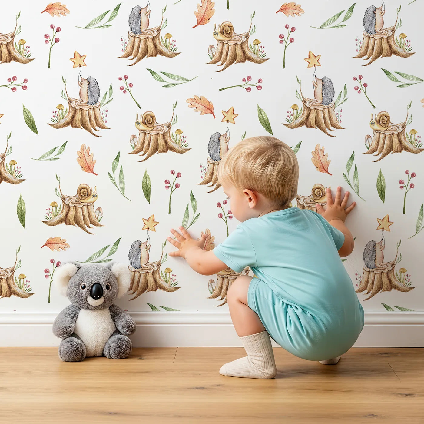 Lovely child standing in front of Whimsy Tots Forest Stump Snuggle Wallpaper in White with hedgehog, snail, tree stump, star, oak leaf, berry, leaf, mushroom in design.