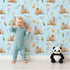 Lovely child standing in front of Whimsy Tots Forest Stump Snuggle Wallpaper in Blue with hedgehog, snail, tree stump, star, oak leaf, berry, leaf, mushroom in design.