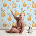 Lovely child standing in front of Whimsy Tots Pumpkin Patch Whimsy Wallpaper in Blue with pumpkin, bird, heart, leaf in design.