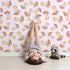 Lovely child standing in front of Whimsy Tots Mushroom Meadow Whispers Wallpaper in Blush Pink with mushroom, meadow, whispers, wallpaper in design.
