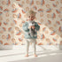 Lovely child standing in front of Whimsy Tots Mushroom Meadow Whispers Wallpaper in Cream with mushroom in design.