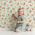 Lovely child standing in front of Whimsy Tots Mushroom Meadow Whispers Wallpaper in Mint Green with mushroom, meadow, whispers, wallpaper in design.