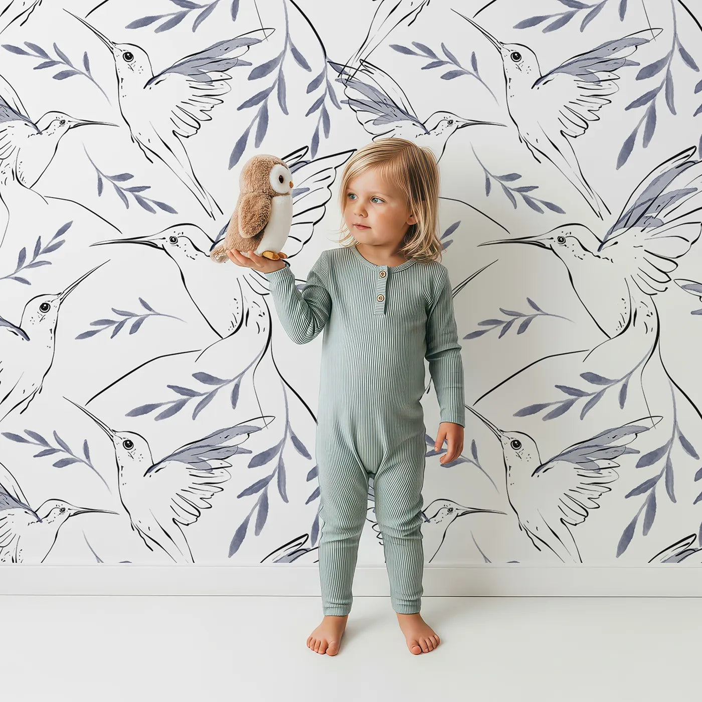 Lovely child standing in front of Whimsy Tots Hummingbird Line Dance Wallpaper in Ink Leaf with bird, hummingbird, leaf in design.