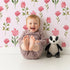 Lovely child standing in front of Whimsy Tots Pink Meadow Blossoms Wallpaper in Blush with flower, leaf in design.