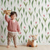 Lovely child standing in front of Whimsy Tots Tulip Meadow Dots Wallpaper in White with flower, leaf, tulip in design.