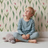 Lovely child standing in front of Whimsy Tots Tulip Meadow Dots Wallpaper in Cream with flower, leaf, tulip in design.