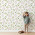 Lovely child standing in front of Whimsy Tots Botanical Berry Sprigs Wallpaper in White with berry, leaf, sprig in design.