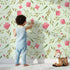 Lovely child standing in front of Whimsy Tots Blushing Petal Tangle Wallpaper in Mint Green with flower, leaf, petal, vine in design.