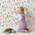 Lovely child standing in front of Whimsy Tots Berry Leaf Doodle Wallpaper in White with berry, leaf, branch, dot in design.