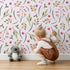 Lovely child standing in front of Whimsy Tots Berry Leaf Doodle Wallpaper in Blush Pink with berry, leaf, branch, dot in design.