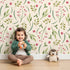 Lovely child standing in front of Whimsy Tots Berry Leaf Doodle Wallpaper in Cream with berry, leaf, branch, dot in design.