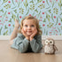 Lovely child standing in front of Whimsy Tots Berry Leaf Doodle Wallpaper in Sky with berry, leaf, branch, dot in design.