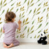 Lovely child standing in front of Whimsy Tots Wandering Willow Sprigs Wallpaper in White with leaf, sprig, branch in design.
