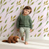 Lovely child standing in front of Whimsy Tots Wandering Willow Sprigs Wallpaper in Blush Pink with leaf, sprig, branch in design.