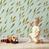 Lovely child standing in front of Whimsy Tots Wandering Willow Sprigs Wallpaper in Mint Green with leaf, sprig, branch in design.