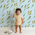 Lovely child standing in front of Whimsy Tots Wandering Willow Sprigs Wallpaper in Sky with leaf, sprig, branch in design.
