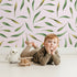 Lovely child standing in front of Whimsy Tots Whimsy Leaf Scatter Wallpaper in Blush Pink with leaf, spray, greenery, foliage in design.