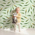 Lovely child standing in front of Whimsy Tots Whimsy Leaf Scatter Wallpaper in Mint Green with leaf, spray, greenery, foliage in design.