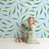 Lovely child standing in front of Whimsy Tots Whimsy Leaf Scatter Wallpaper in Sky with leaf, spray, greenery, foliage in design.