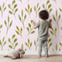 Lovely child standing in front of Whimsy Tots Whimsy Leaf Branch Wallpaper in Blush Pink with leaf, stem, greenery, branch in design.