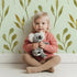 Lovely child standing in front of Whimsy Tots Whimsy Leaf Branch Wallpaper in Mint Green with leaf, stem, greenery, branch in design.