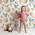Lovely child standing in front of Whimsy Tots Moon Melody Wallpaper in White with bird, moon, heart, star in design.