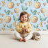 Lovely child standing in front of Whimsy Tots Moon Melody Wallpaper in Sky with bird, moon, heart, star in design.