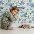 Lovely child standing in front of Whimsy Tots Sleepy Ocean Friends Wallpaper in Mint Green with whale, narwhal, fish, sea in design.