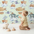 Lovely child standing in front of Whimsy Tots Sky Explorers Wallpaper in Mint Green with fish, submarine, balloon, ship, sky, cloud in design.