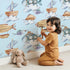 Lovely child standing in front of Whimsy Tots Sky Explorers Wallpaper in Sky Blue with fish, submarine, balloon, ship, sky, cloud in design.