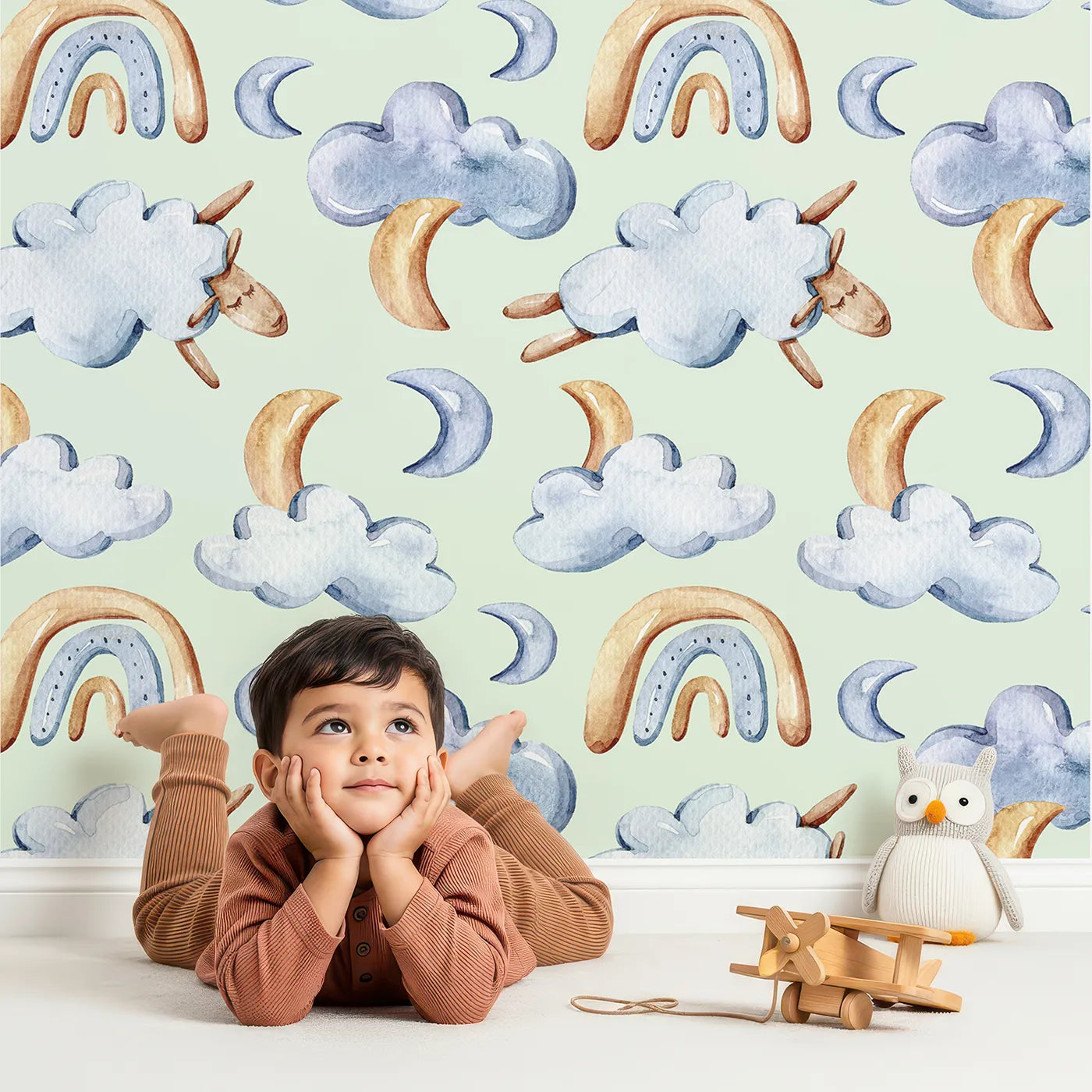 Lovely child standing in front of Whimsy Tots Sleepy Skies Wallpaper in Mint Green with cloud, moon, rainbow, sheep in design.