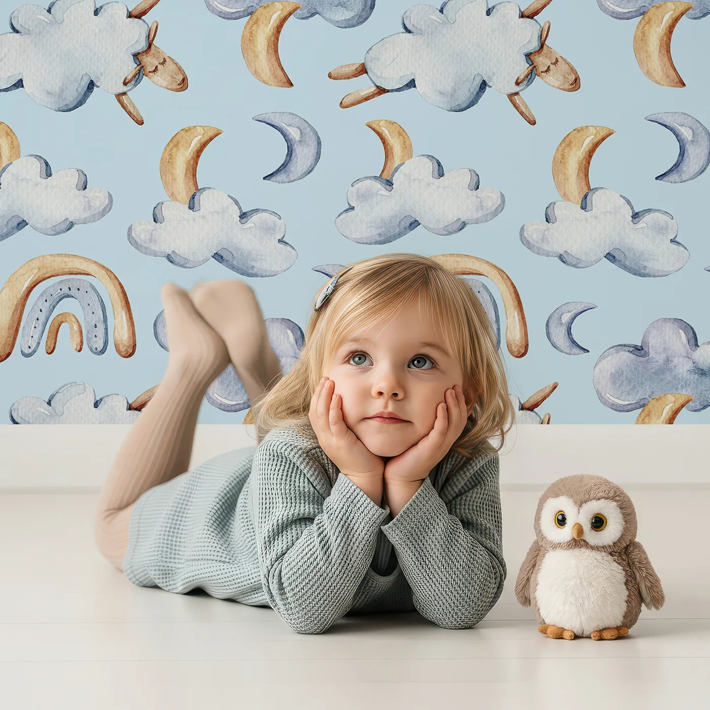 Lovely child standing in front of Whimsy Tots Sleepy Skies Wallpaper in Blue with cloud, moon, rainbow, sheep in design.