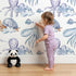Lovely child standing in front of Whimsy Tots Ocean Dreams Wallpaper in White with cloud, turtle, octopus, squid, fish in design.