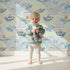 Lovely child standing in front of Whimsy Tots Whale Boat Parade Wallpaper in Mint Green with whale, submarine, boat, octopus, anchor, flag in design.
