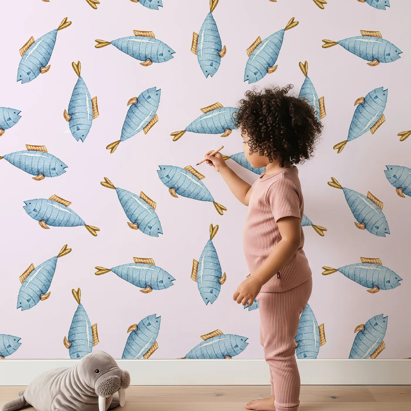 Lovely child standing in front of Whimsy Tots Little Swimmer Fish Wallpaper in Pink with fish in design.