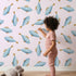 Lovely child standing in front of Whimsy Tots Little Swimmer Fish Wallpaper in Pink with fish in design.